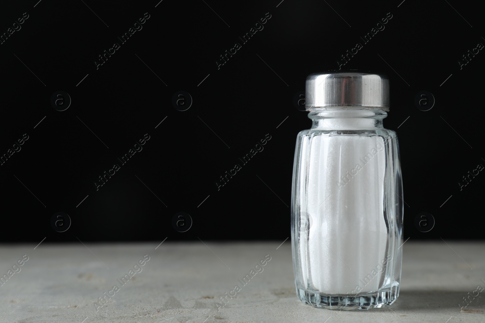 Photo of Salt shaker on light table against black background. Space for text