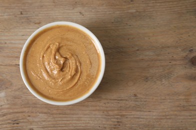 Photo of Delicious nut butter in bowl on wooden table, top view. Space for text