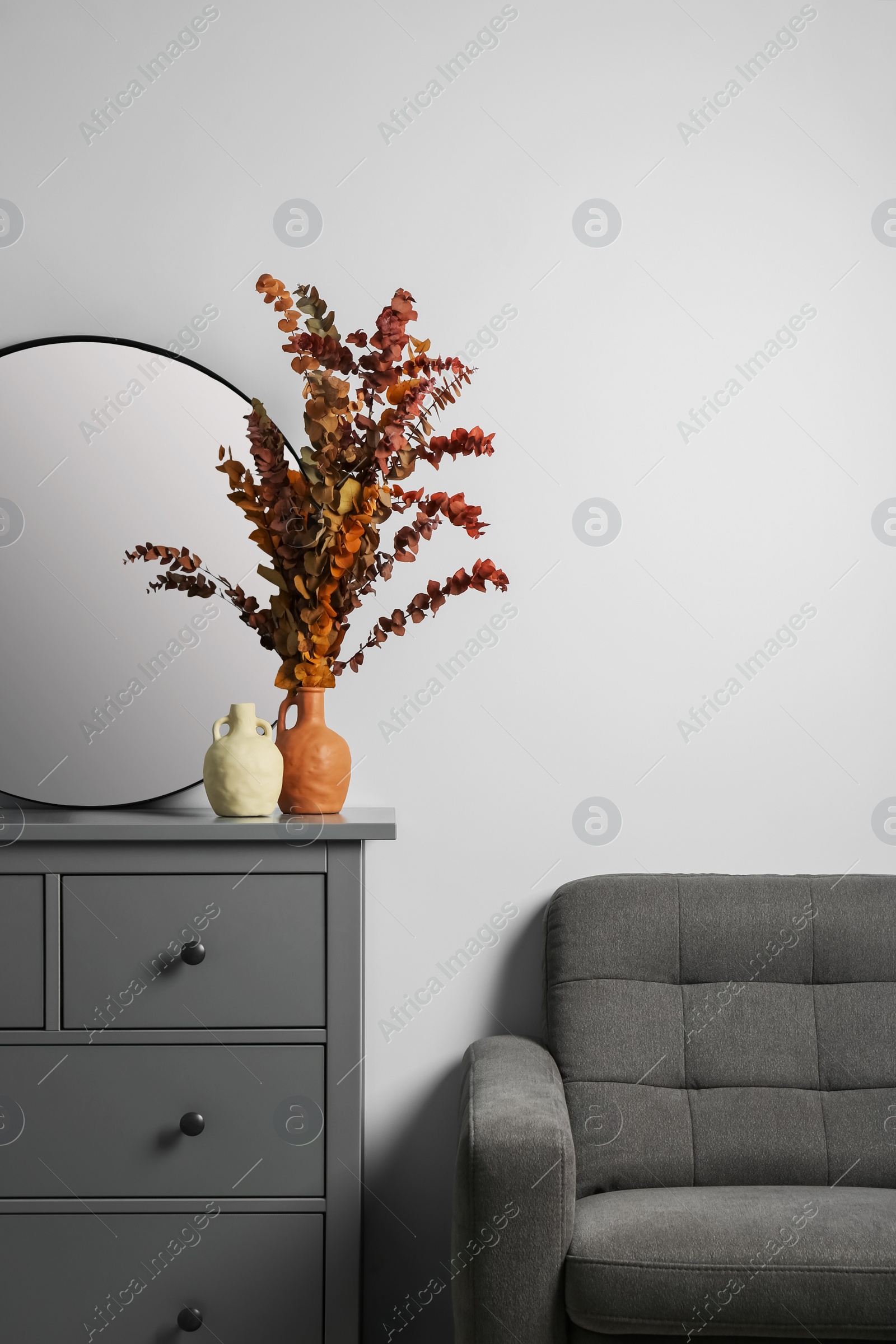 Photo of Grey chest of drawers with decor and armchair near white wall in room, space for text. Interior design