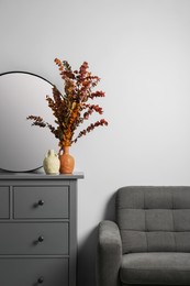 Grey chest of drawers with decor and armchair near white wall in room, space for text. Interior design