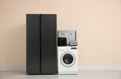 Modern refrigerator and other household appliances near beige wall indoors