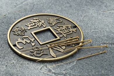 Photo of Acupuncture needles and Chinese coin on grey textured table, closeup