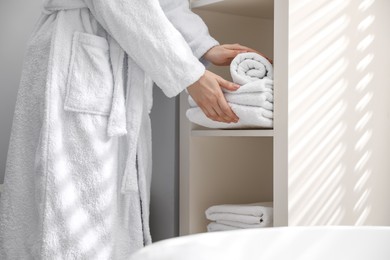 Photo of Woman stacking clean towels on shelf in bathroom, closeup
