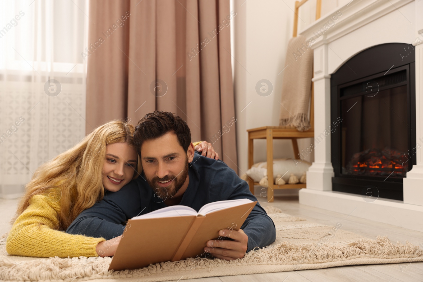 Photo of Lovely couple reading book near fireplace at home