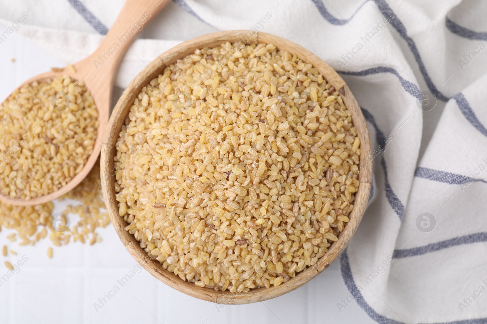 Photo of Bowl and spoon with raw bulgur on table, flat lay