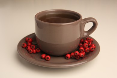 Aromatic hawthorn tea in cup and berries on beige table, closeup