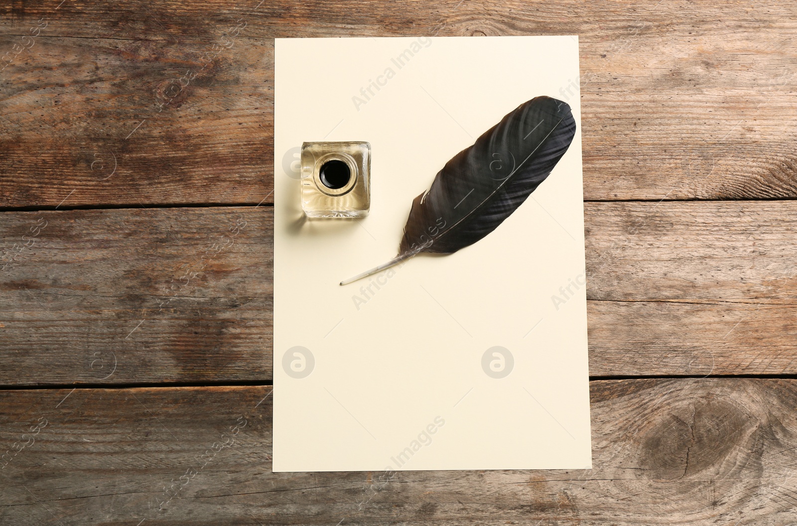 Photo of Feather pen, inkwell and blank parchment on wooden table, top view. Space for text