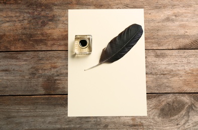Feather pen, inkwell and blank parchment on wooden table, top view. Space for text