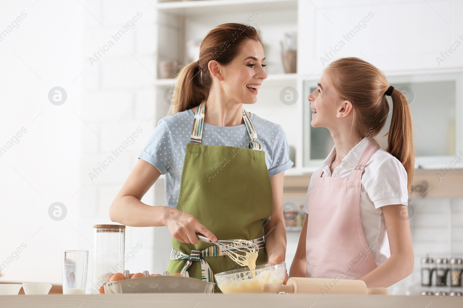 Photo of Mother and her daughter making dough at table in kitchen