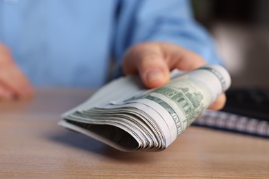 Money exchange. Woman holding dollar banknotes at wooden table, closeup