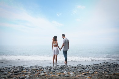 Photo of Young couple spending time together on beach near sea, back view