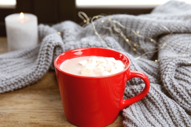 Photo of Cup of hot cocoa with marshmallows and sweater on window sill. Winter drink