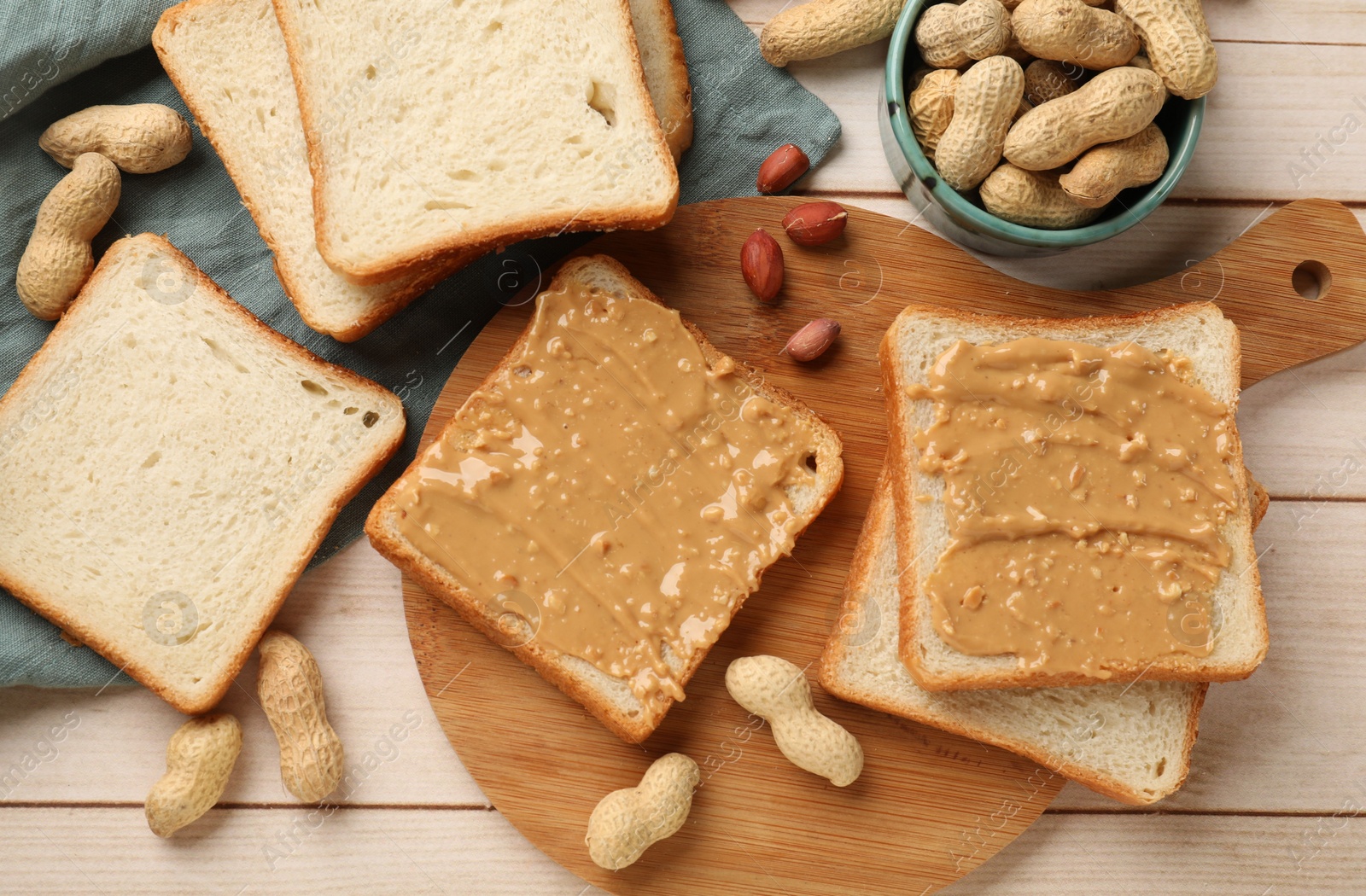 Photo of Delicious toasts with peanut butter and nuts on light wooden table, flat lay