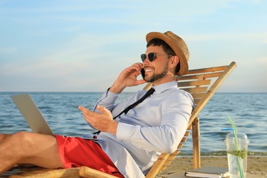 Man with laptop talking by mobile phone on beach. Business trip