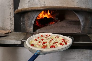 Photo of Putting tasty pizza into oven in  restaurant kitchen