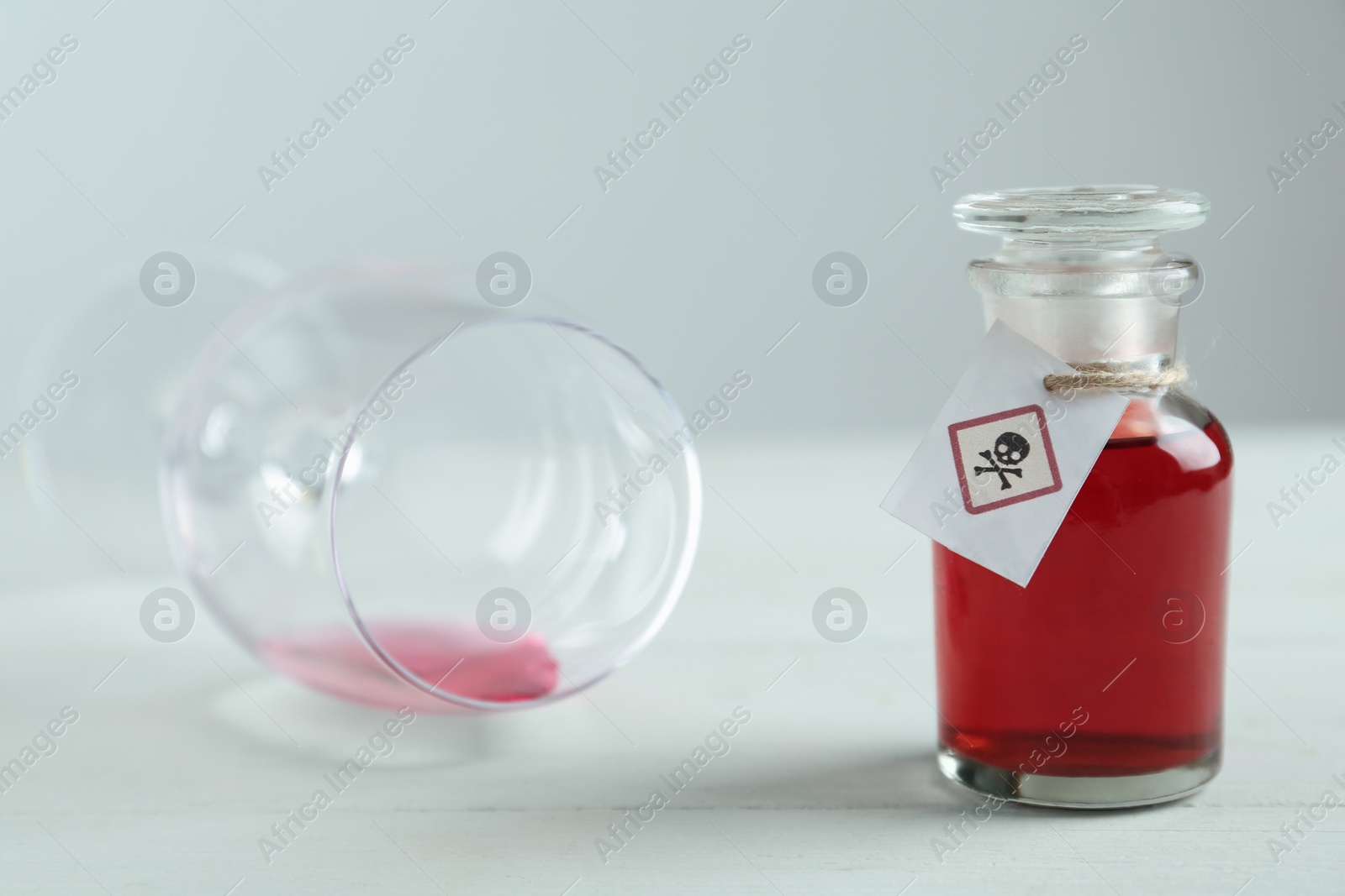 Photo of Bottle of poison and partially emptied glass on light background