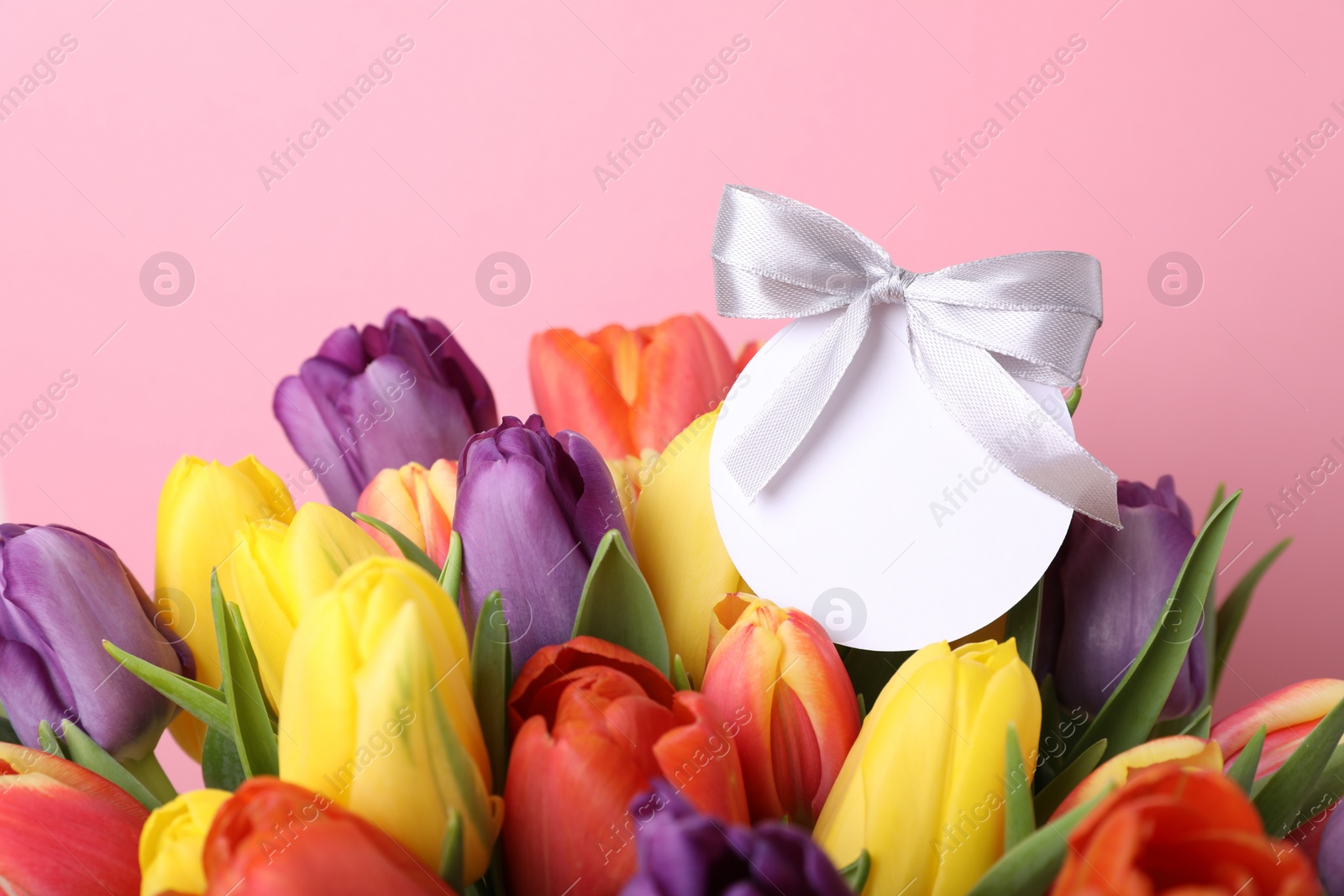 Photo of Bouquet of beautiful colorful tulips with blank card on pink background, closeup. Birthday celebration