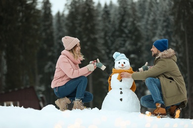 Couple making snowman near forest. Winter vacation