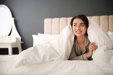 Photo of Beautiful young woman wrapped with soft blanket relaxing in bed at home