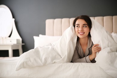 Beautiful young woman wrapped with soft blanket relaxing in bed at home