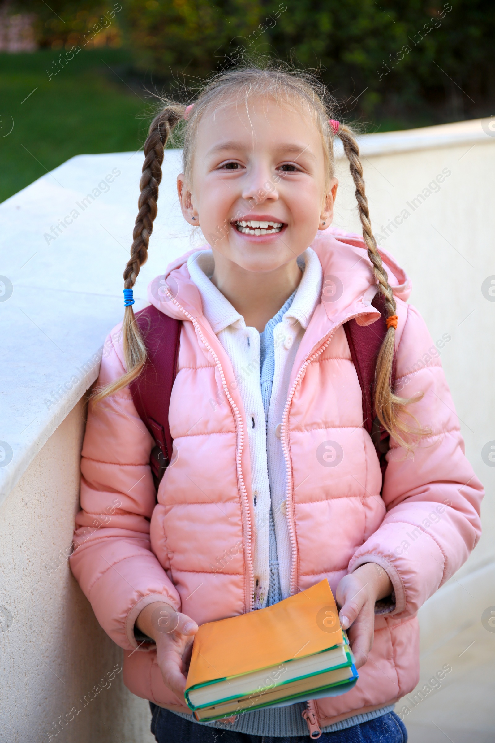 Photo of Cute little girl with backpack and textbooks outdoors