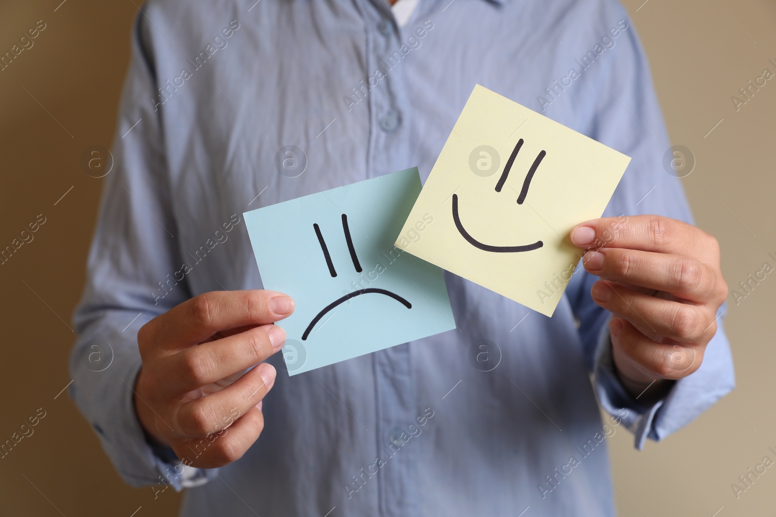 Photo of Choice concept. Woman holding papers with sad and happy emoticons on beige background, closeup