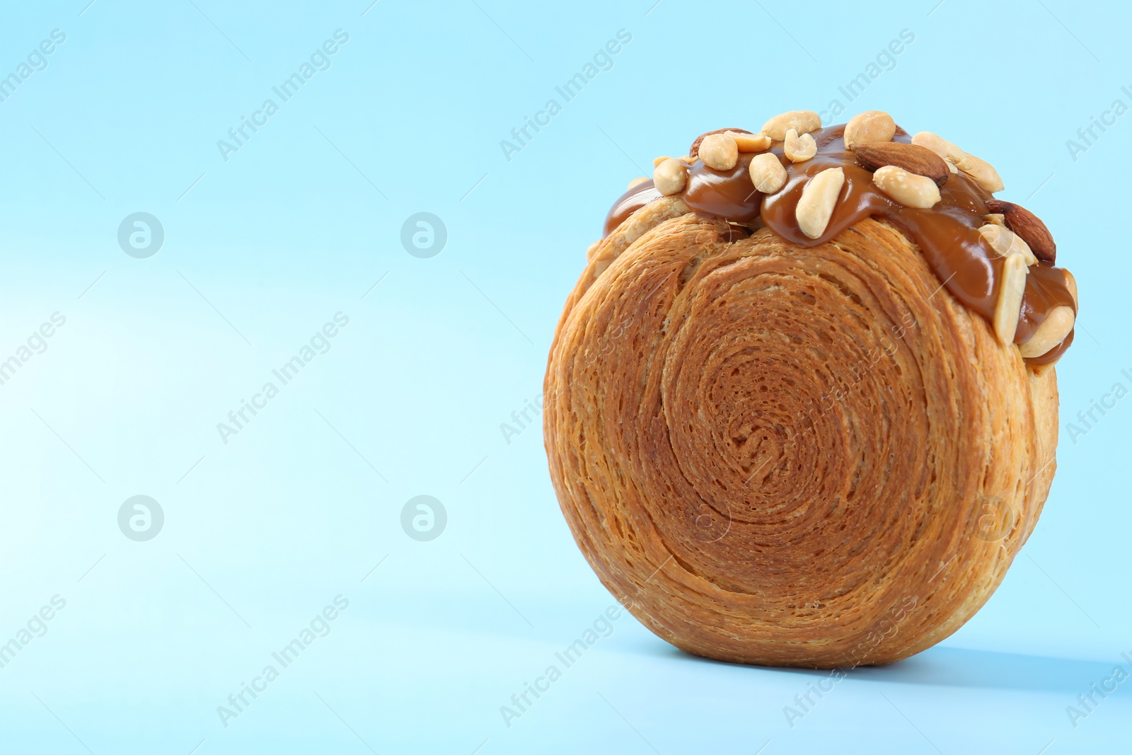 Photo of One supreme croissant with chocolate paste and nuts on light blue background, closeup with space for text. Tasty puff pastry