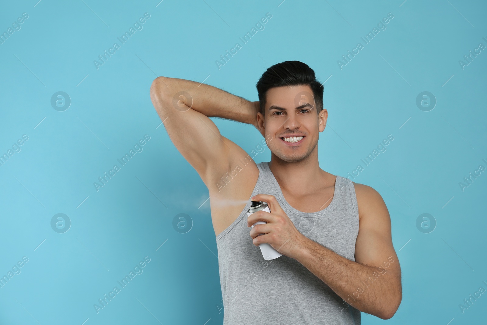 Photo of Handsome man applying deodorant to armpit on turquoise background, space for text