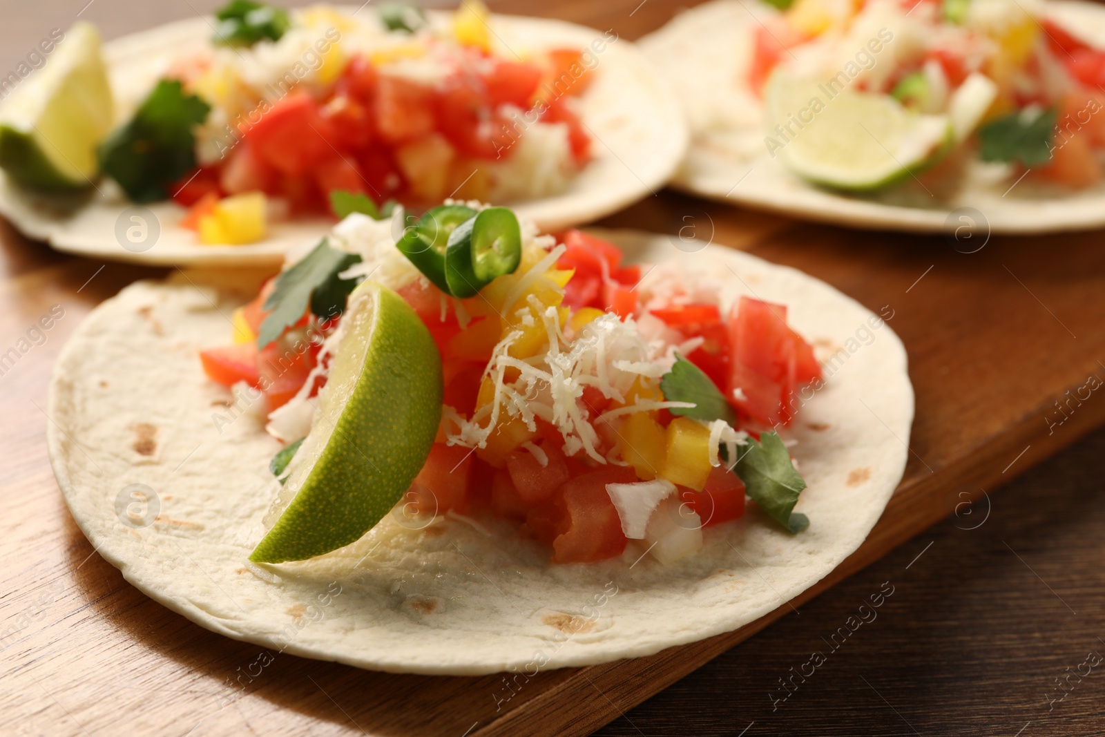 Photo of Delicious tacos with vegetables and lime on wooden table, closeup