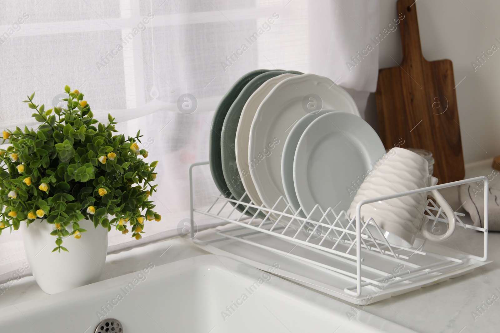 Photo of Drainer with different clean dishware, cup and houseplant on light table indoors