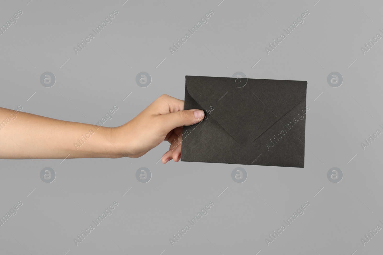Photo of Woman holding black paper envelope on light grey background, closeup