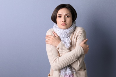 Photo of Young woman in warm clothes suffering from cold on color background