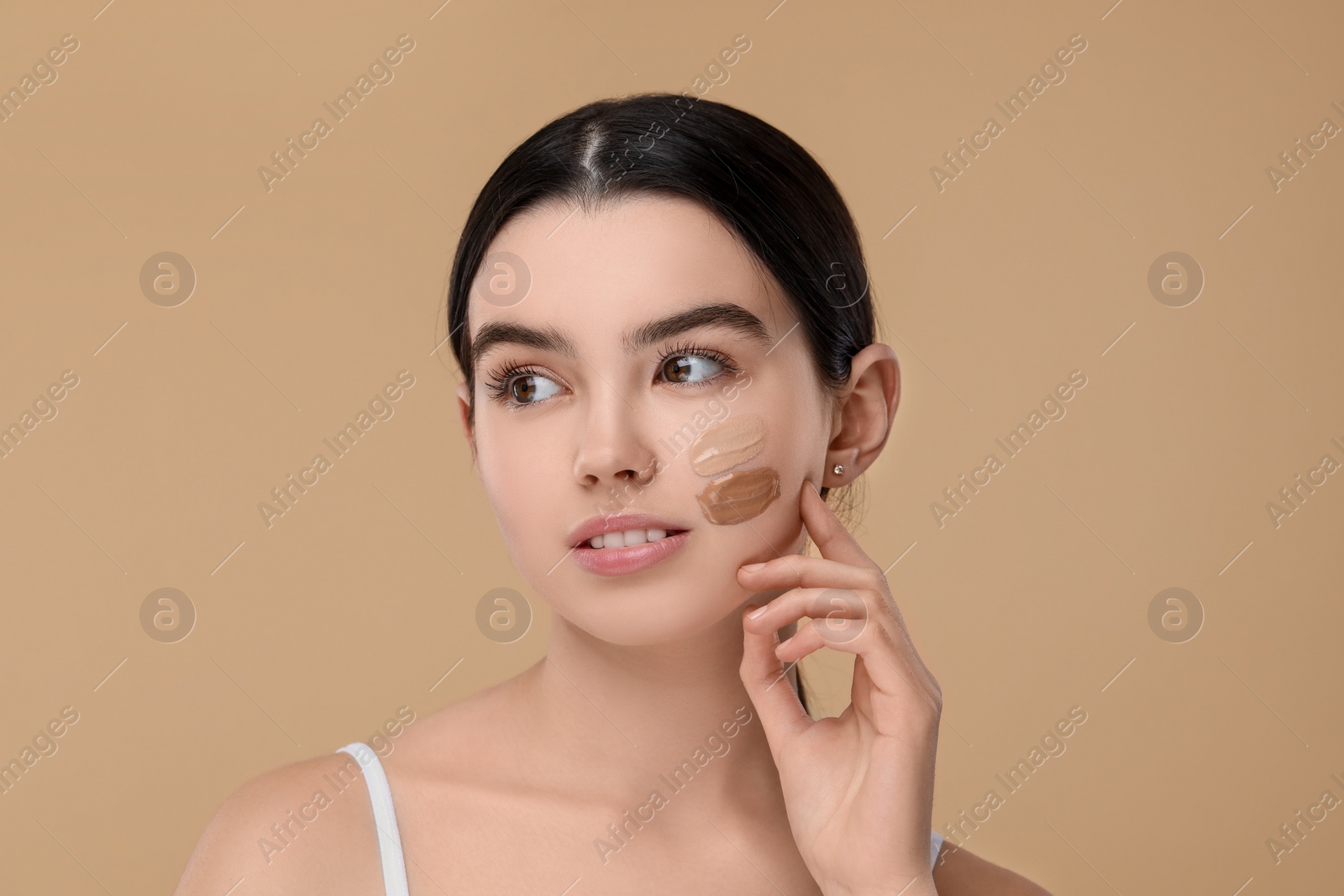 Photo of Teenage girl with swatches of foundation on face against beige background