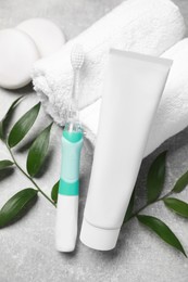 Photo of Electric toothbrush, tube of paste and rolled towels on grey textured table, closeup