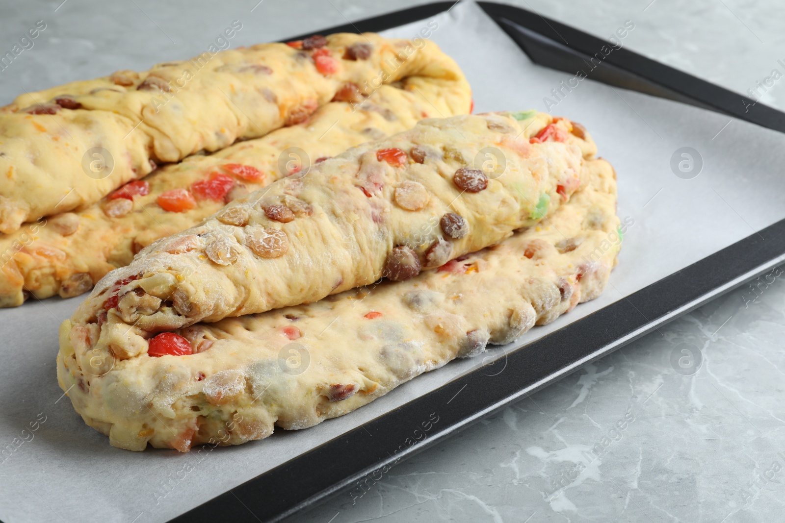 Photo of Baking tray with raw homemade Stollens on grey marble table, closeup. Traditional German Christmas bread