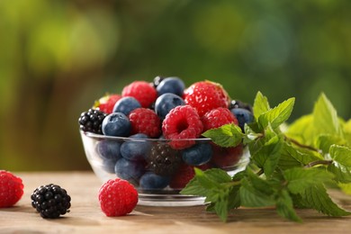 Photo of Glass bowl with different fresh ripe berries and mint on wooden table outdoors