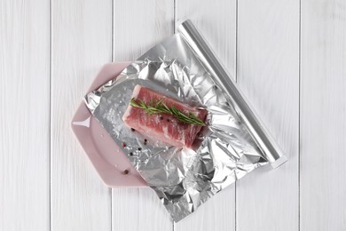 Aluminum foil with raw meat, rosemary and spices on white wooden table, top view