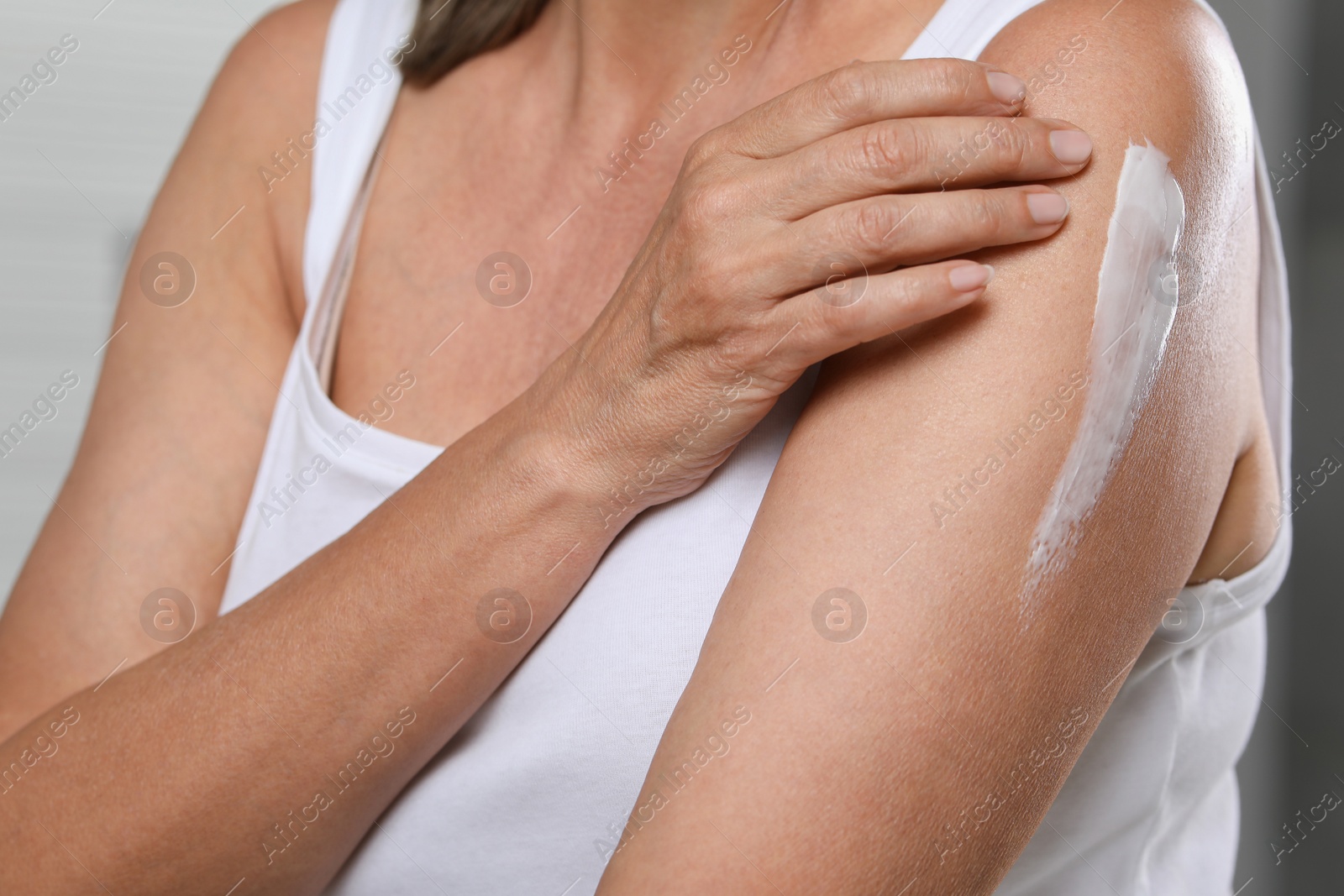Photo of Woman applying body cream onto arm on blurred background, closeup