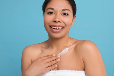 Photo of Young woman applying cream onto body on light blue background