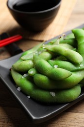 Black plate with green edamame beans in pods on wooden table, closeup