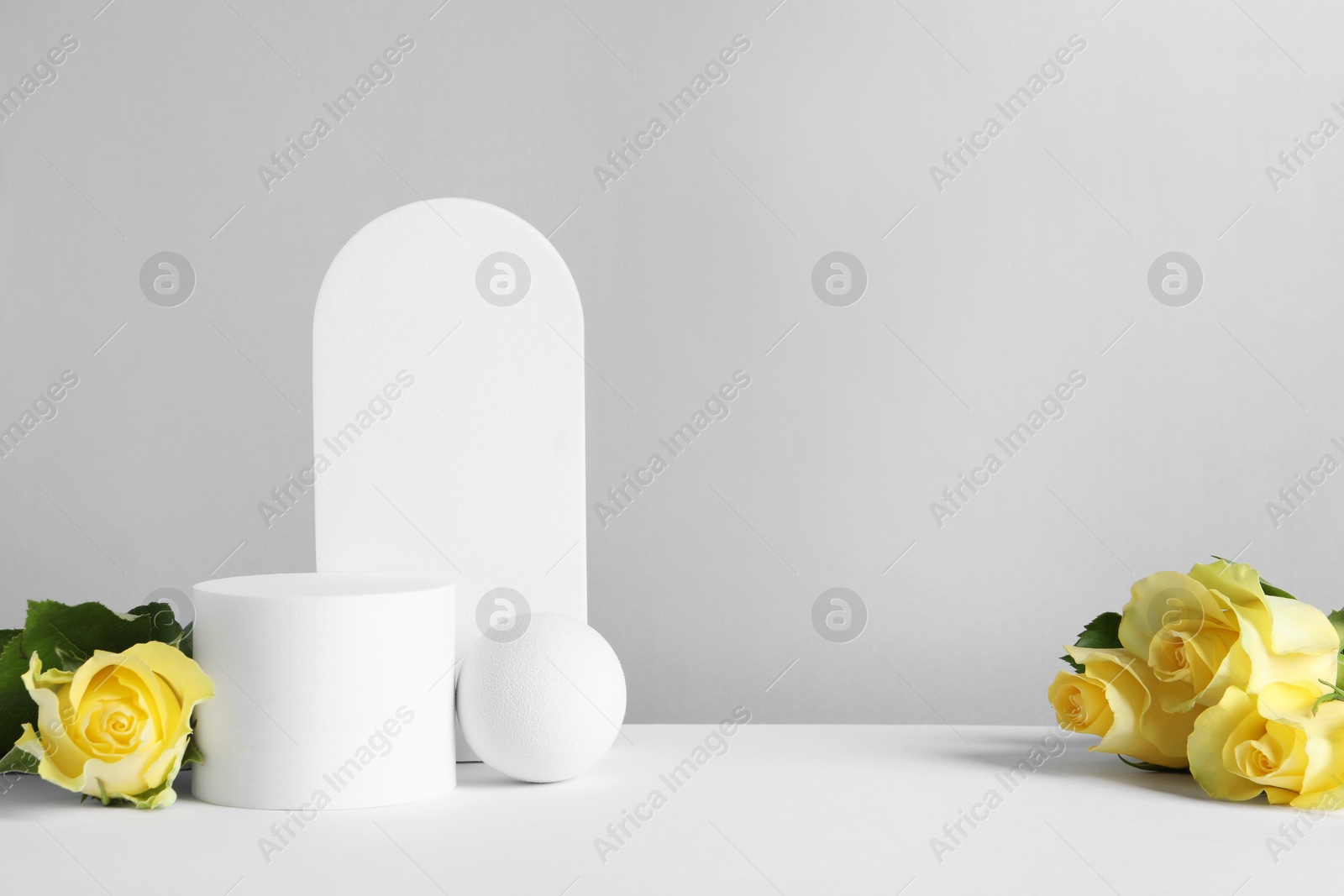 Photo of Beautiful presentation for product. Geometric figures and yellow roses on white table against light grey background, space for text