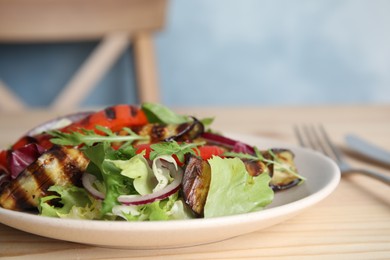 Photo of Delicious salad with roasted eggplant and arugula served on wooden table, closeup