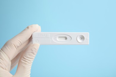 Photo of Doctor holding disposable express test for hepatitis on light blue background, closeup