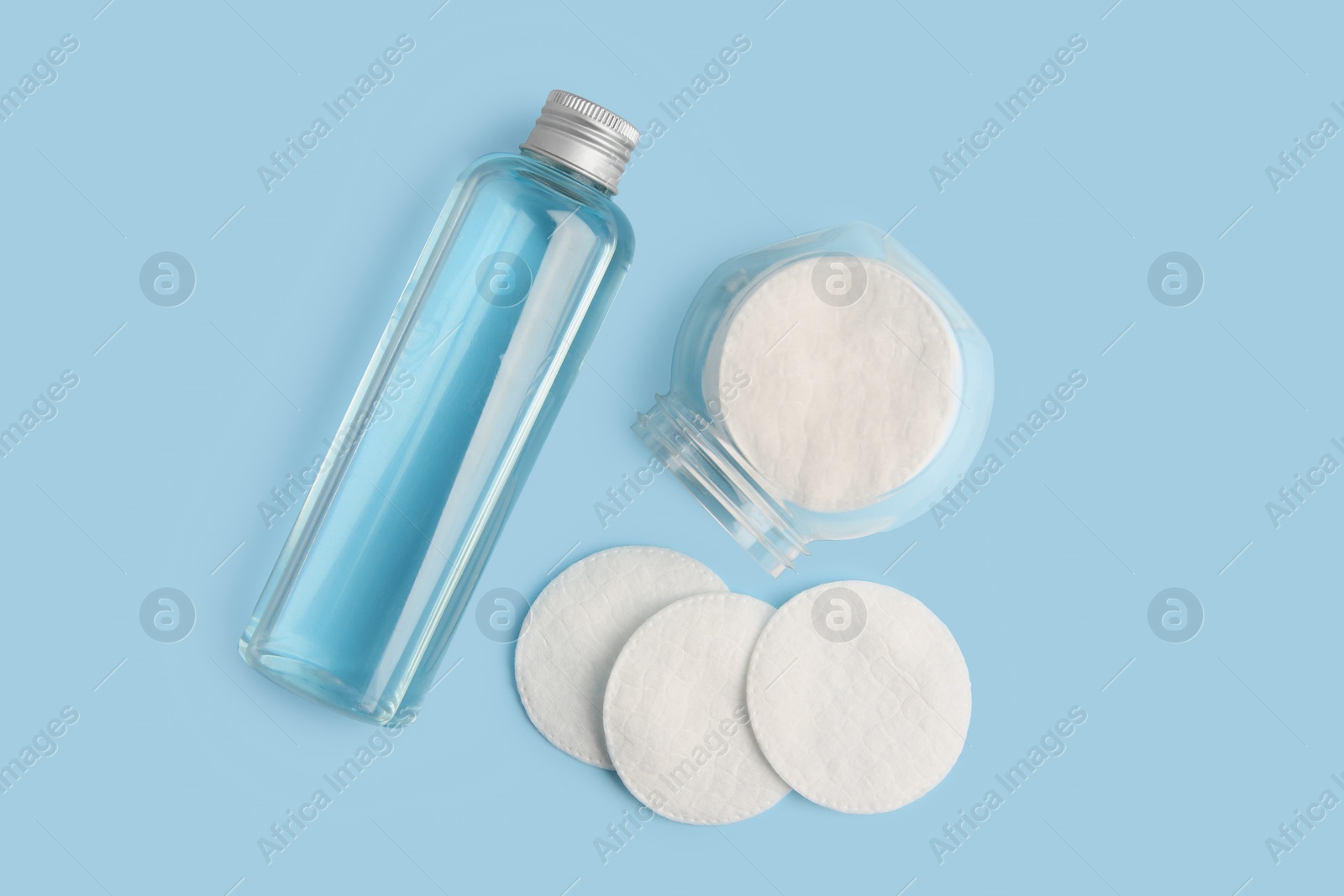 Photo of Bottle of makeup remover and cotton pads on light blue background, flat lay