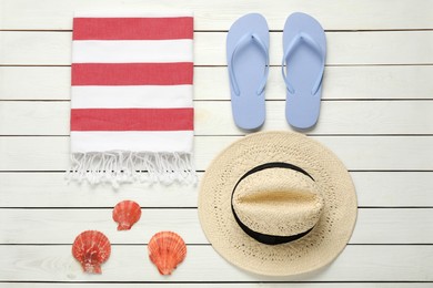 Beach towel, flip flops, straw hat and seashells on white wooden background, flat lay
