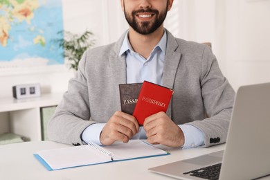 Happy manager holding passports at desk in travel agency, closeup