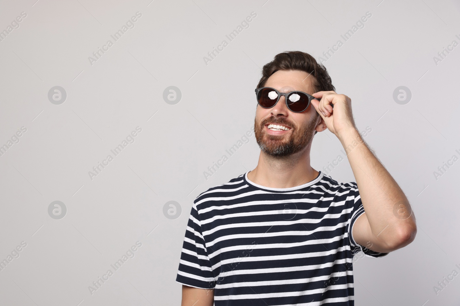 Photo of Portrait of smiling bearded man with stylish sunglasses on light grey background. Space for text