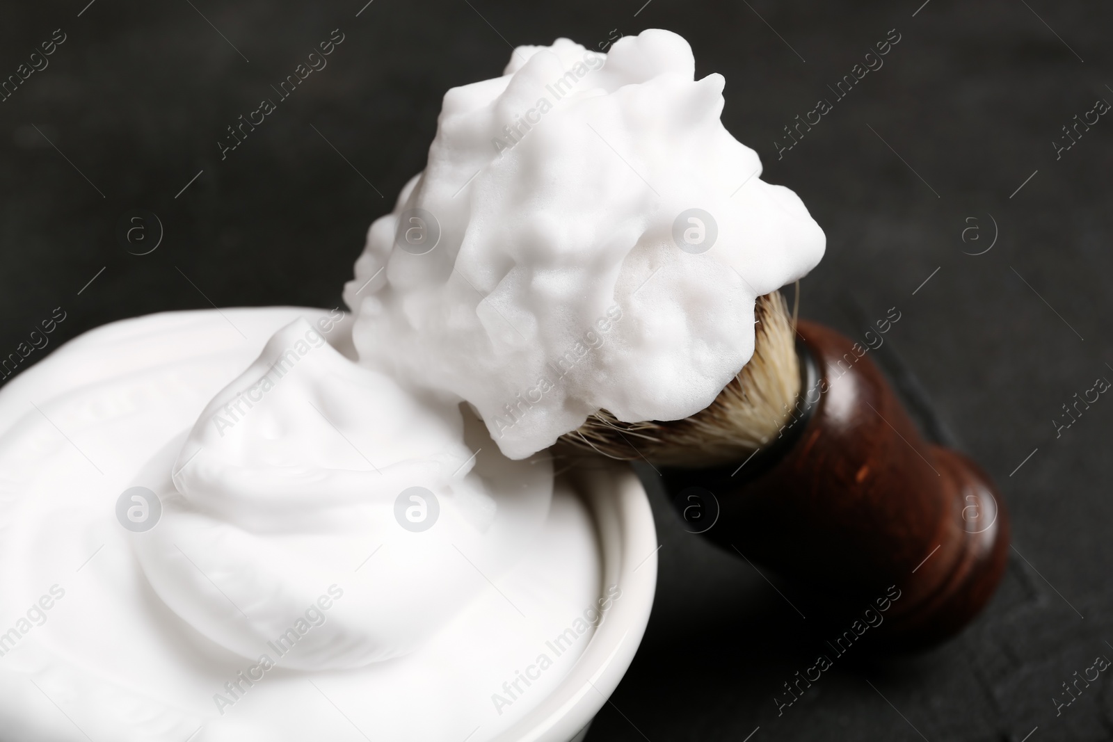 Photo of Shaving brush and bowl of foam on dark background