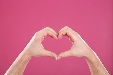 Photo of Man making heart with his hands on color background, closeup