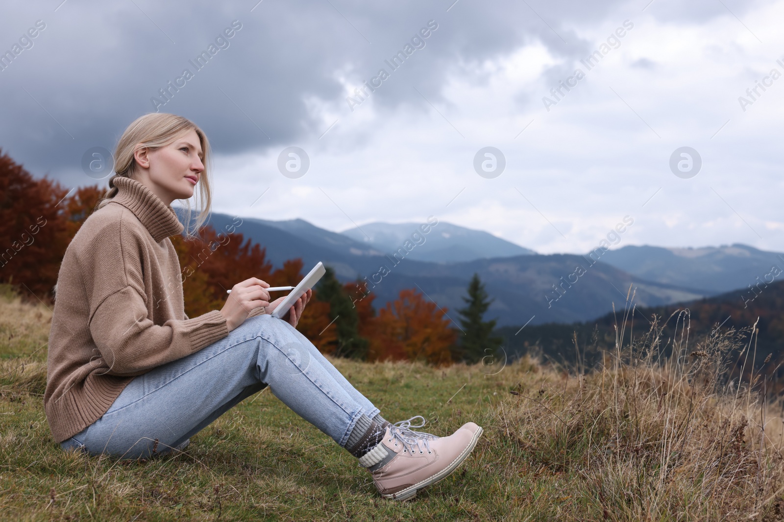 Photo of Young woman drawing on tablet in mountains, space for text